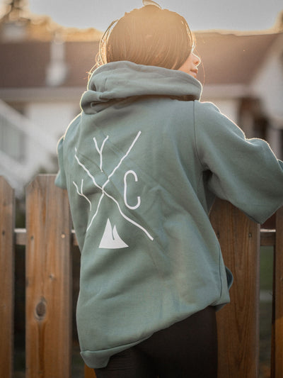Individual outside wearing the Local Laundry YYC hoodie in sage green, showcasing the Local Laundry trademark YYC graphic on the back of the hoodie. This hoodie is proudly and sustainably made in Canada.