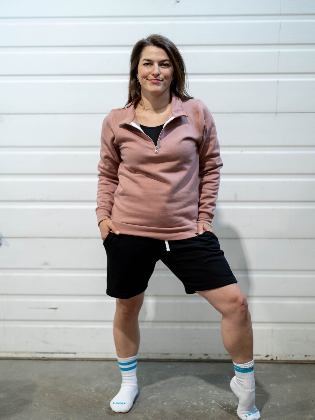 Individual wearing made in Canada Local Laundry 3/4 zip sweater in dusty rose, paired with black Local Laundry sweat shorts and a pair of white and blue Local Laundry giving socks
