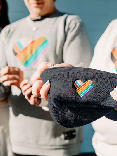 Individual holding a made in Canada Pride toque, radiating pride with a vibrant rainbow heart on the toque