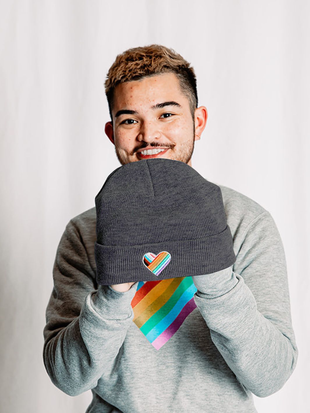Individual holding a made in Canada Pride toque, radiating pride with a vibrant rainbow heart on the front cuff of the toque.