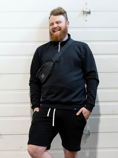 stylish individual wearing sustainable Canadian made black 1/4 zip sweater with black Canadian made sweat shorts. Along with a functional Made in Canada Fanny Pack.