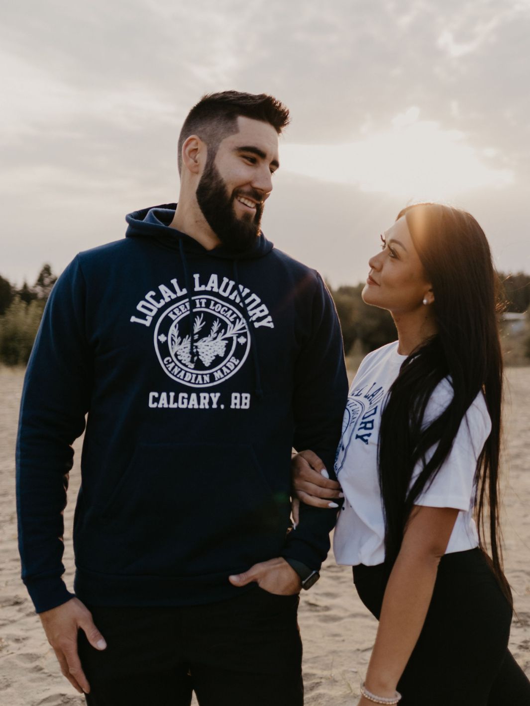 Individuals wearing their varsity line clothing by Local Laundry. One individual is wearing the Varsity Hoodie in Navy Blue, and the other wearing the white varsity t-shirt.