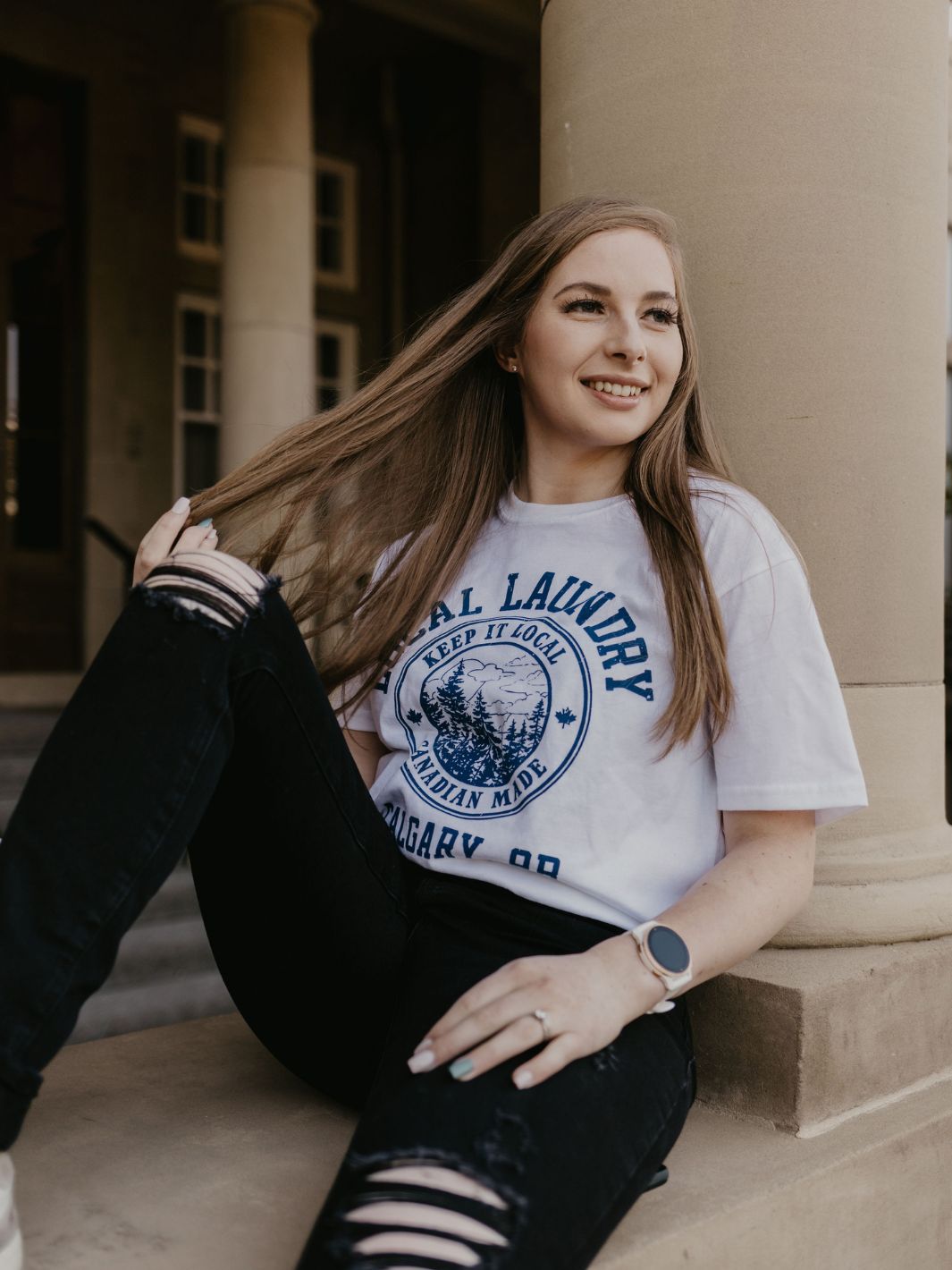 individual hanging out downtown in their Varsity t-shirt by Local Laundry. This white t-shirt features a contrasting blue crest graphic on the front. Made in Canada utilizing a premium 50/50 blend of cotton and polyester