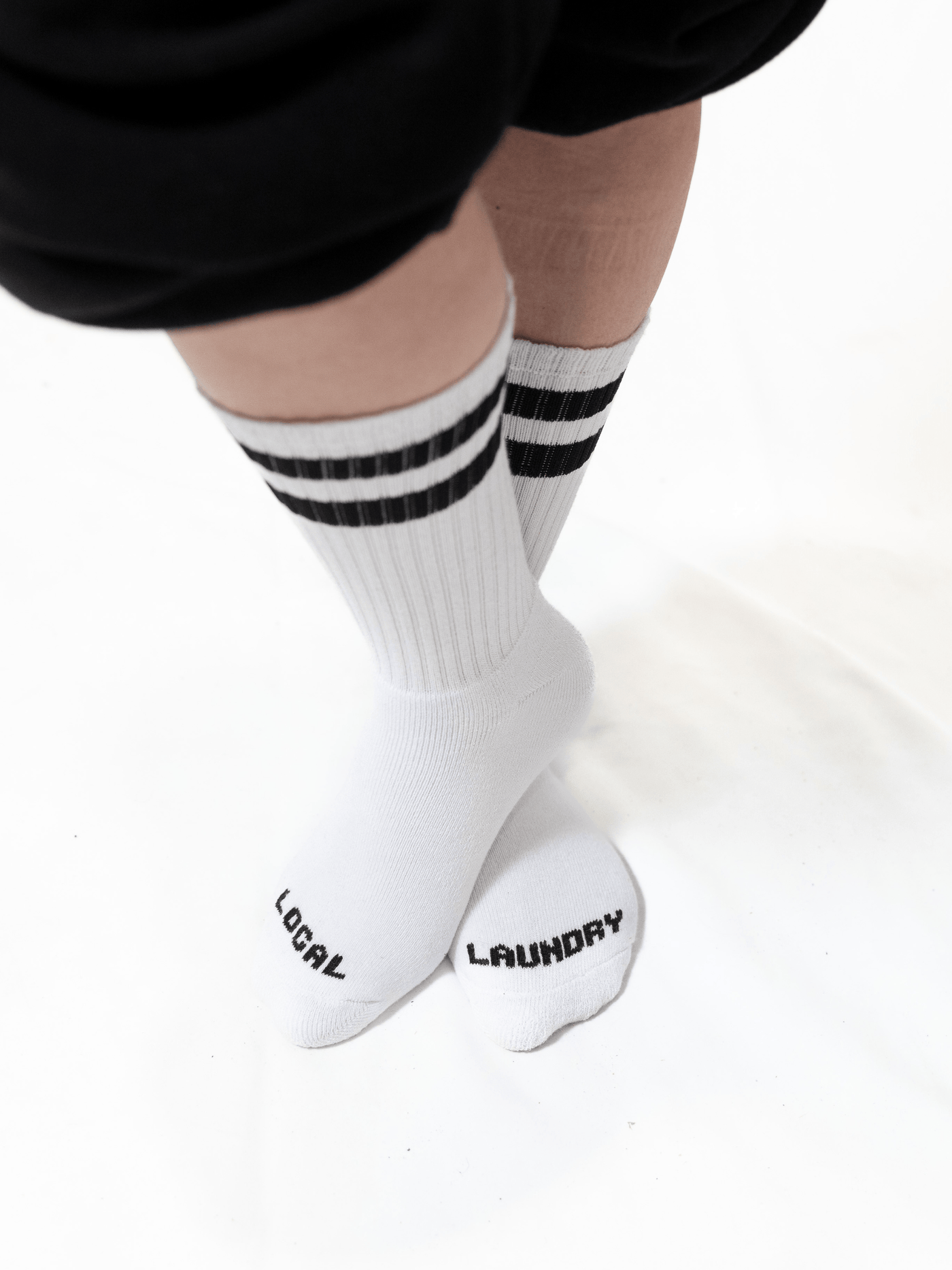 The Local Laundry Giving Sock, white with black contrast stripes and the phrase "Local" and "Laundry" across each foot. These socks are made in Canada and all proceeds go towards giving socks to charities.