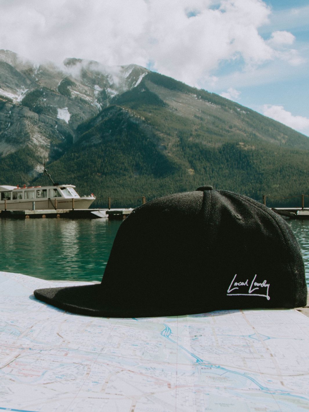 The Local Laundry Rundle snapback hat, resting atop a road map with a lake and mountains in the background. This hat is sustainably made in Vancouver, BC Canada.