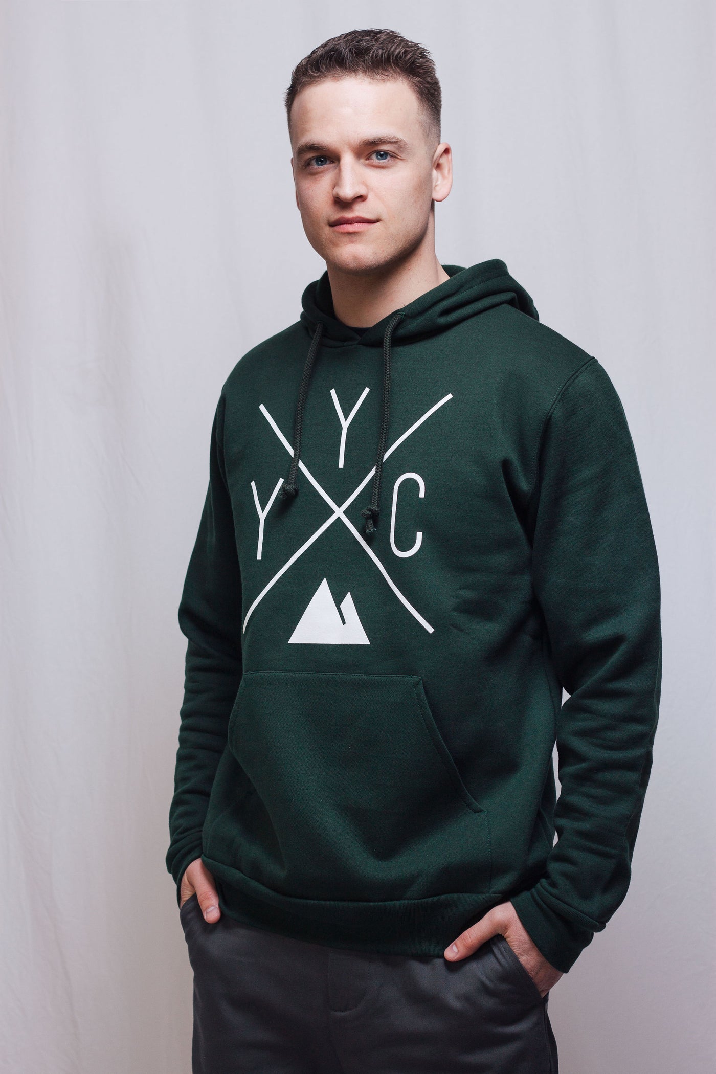 Individual wearing forest green YYC Hoodie. The individual is painting this hoodie with charcoal trousers. Made in Canada, sustainably.
