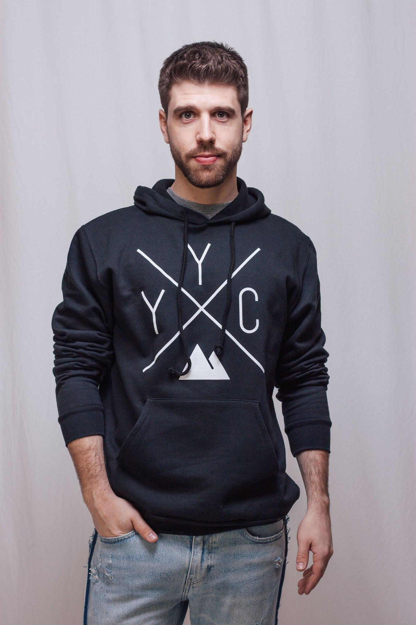 Individual wearing the Local Laundry YYC Hoodie in black, featuring a white YYC graphic trademarked by Local Laundry. Individual is wearing this hoodie with a pair of blue denim. Sustainably made in Canada, represents supporting local economies.
