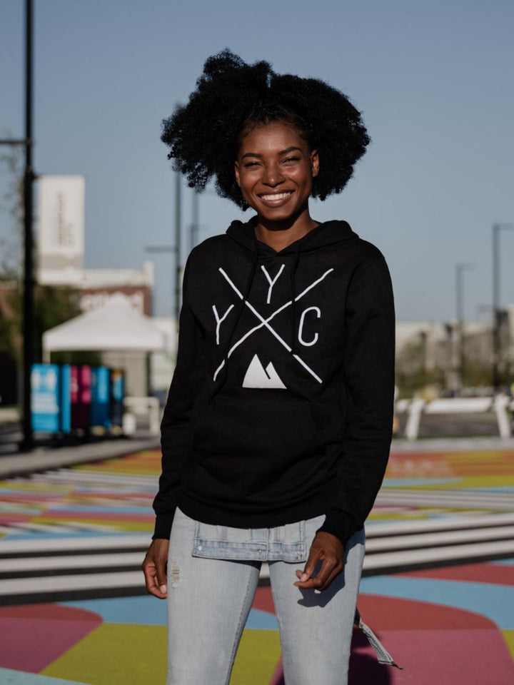 Happy individual wearing black YYC hoodie by Local Laundry in front of a multicoloured mosaic in Calgary AB. 